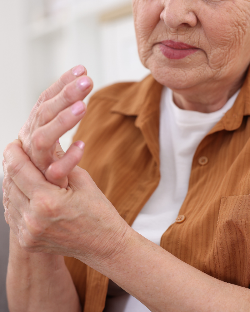 Senior woman holding her right hand and wrist with her left, seemingly in pain. Photo by Africa images, sourced from Canva.